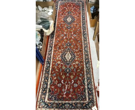 An Oriental runner, the central panel set with two medallions on a rust red ground with scrolling decoration, within a steppe