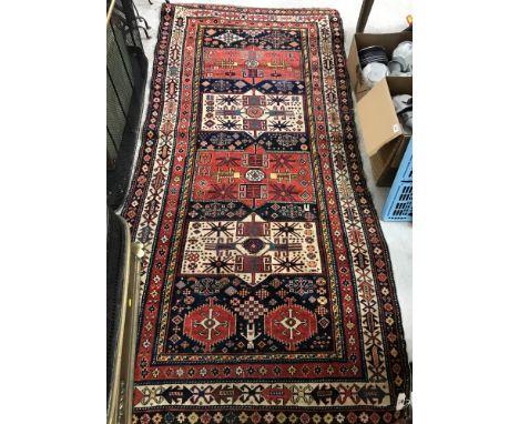 A vintage Caucasian rug, the central panel set with repeating medallions on a blue ground, with stylised figural, animal and 