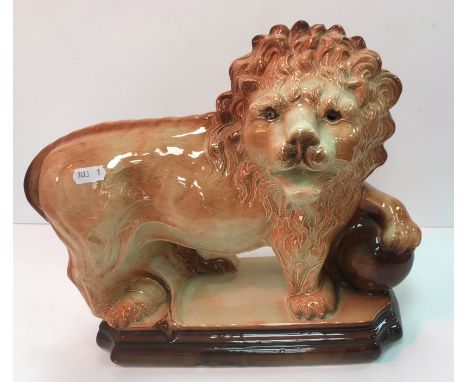 A pair of early 20th Century Staffordshire pottery figures of lions with paws on balls on a plinth base 33 cm long x 27 cm hi