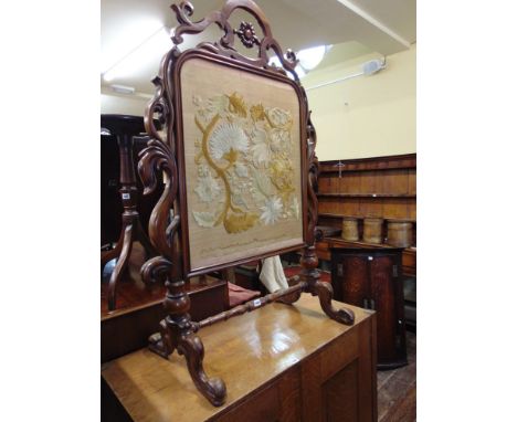 An early 19th century rosewood firescreen with well carved floral borders raised on a stretcher base with hand worked crewel 