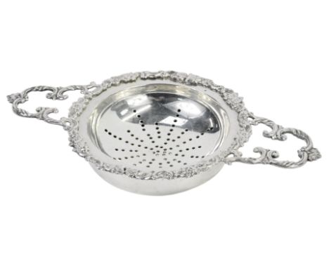 An Elizabeth II silver twin handled tea strainer and stand, the strainer with a floral and scroll border, London 1862, 4.44oz
