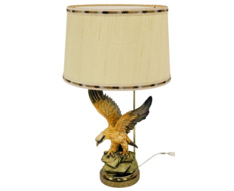 A 20thC table lamp, modelled as an eagle with wings raised, on a rockwork base, on an embossed brass circular base decorated 