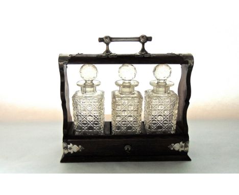 A Victorian oak 3-divisional tantalus containing a trio of clear cut cased decanters with facetted globular stoppers, the tan