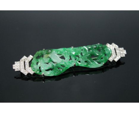 A SPINACH JADE AND DIAMOND ART DECO STYLE BROOCH, the jade carved with exotic birds amongst the foliage, either side is set w