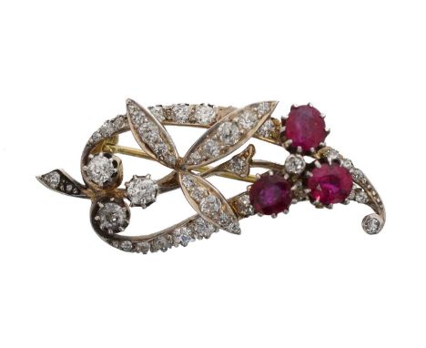 An early 20th century ruby and diamond brooch. The cushion shape ruby tro witin a scrolling and foliate old cut diamond surro