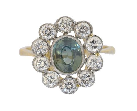 A sapphire and diamond cluster ring. The oval shape green sapphire weighing approx. 1.15cts within a brilliant cut diamond su