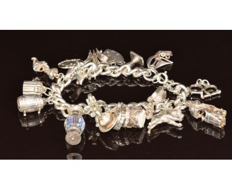 A silver charm bracelet with 18 silver charms including car opening to reveal two horses, boat, barrel opening to reveal a dr