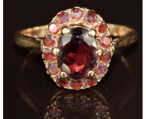 A 9ct gold ring set with an oval cut garnet surrounded by round cut garnets, 3.6g, size R