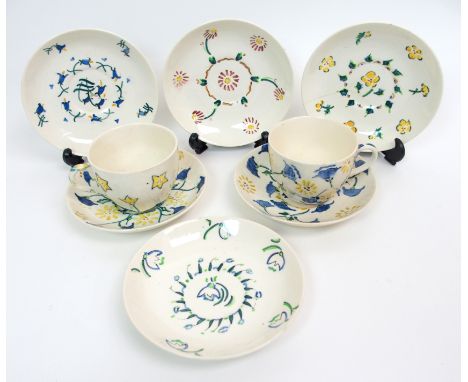 A Jessie M King (1875-1949) pottery cup and saucer painted with blue and yellow flowers on a white ground, another similar sa