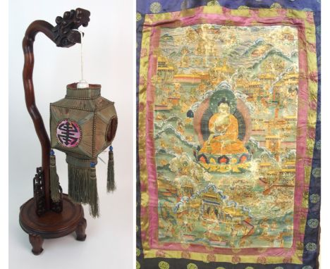A Chinese hardwood table lamp with silk lantern (damages), 69cm high and a Tibetan Thangka decorated with Buddha surrounded b