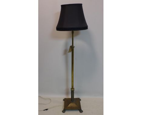 A brass standard lamp, raised on tapered support and four lion paw feet, with black shade, H.155cm 