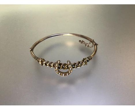 A seed pearl set yellow metal hinged bangle, early 20th century, unmarked, mounted with a horseshoe on a curblink band, with 