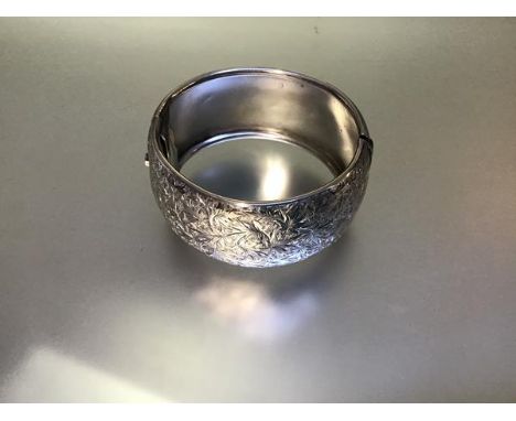 A substantial late Victorian silver cuff bangle, hinged, hollow, engraved with foliate scrollwork, the other half engraved "M