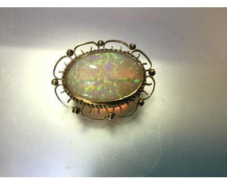 An opal brooch, the large oval opal within a gold wirework frame indistinctly stamped "18ct", with pendant loop fitting. Over