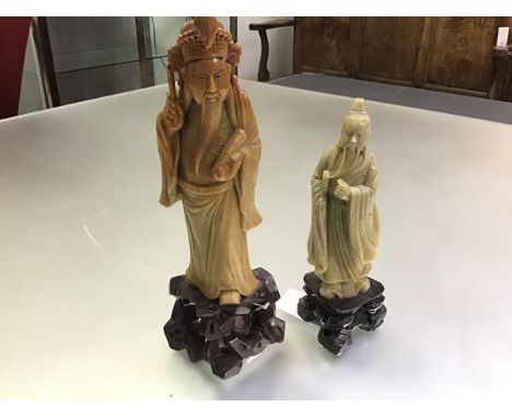 A Chinese soapstone carving of an Immortal, portrayed with scroll and pen, on an integral rock-work base; together with a sma