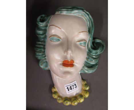 An Art Deco Goldscheider wall mask modelled as the head of a young woman with green hair and eyes, orange lips and yellow nec