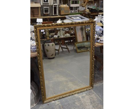 A large gilt framed wall mirror Of rectangular form, with carved leaf detailed frame, with beveled mirror plate. 