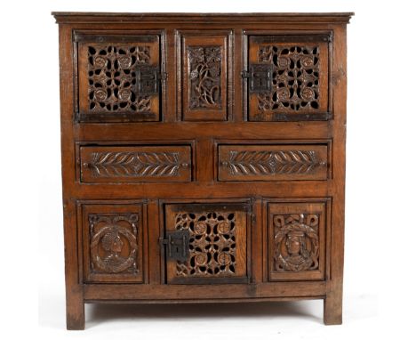 A Tudor oak Aumbry, mid 16th Century, with associated carved panels, the moulded cornice above a pair of pierced carved doors