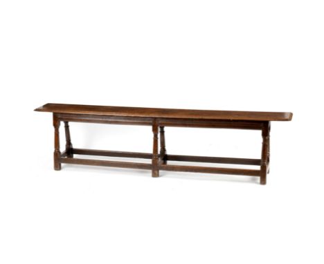 An oak long bench, late 17th Century, the moulded edge single plank top above a moulded frieze on six ring turned tapered leg
