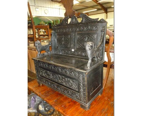 A dark Oak Priory style Bench Seat with carved twin panel back, stylized lion carved arms, on box base with lifting seat and 