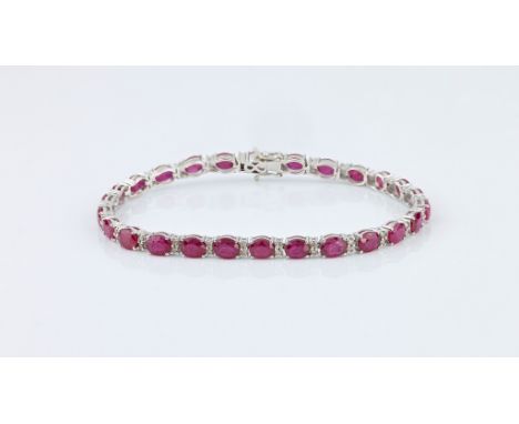 An 18ct white gold, ruby and diamond line bracelet, the twenty-six oval cut rubies totalling 9.30ct, divided by pairs of bril