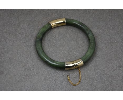 A Chinese jade hinged bangle, late 20th century, with rolled gold fittings chased with bamboo, internal diameter 6.2cm., safe