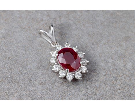 An 18ct white gold, ruby and diamond cluster pendant, the 0.78ct oval cut ruby within a border of twelve brilliant cut diamon