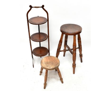A 19th century elm stool, raised on turned column supports, together with a similar smaller example and a mahogany three-tier