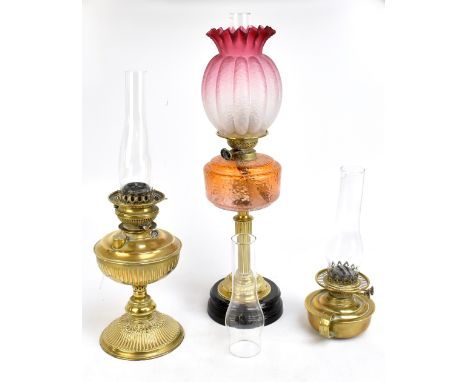 A Victorian brass oil lamp with orange coloured glass reservoir with moulded detail, and two further oil lamps (3).&nbsp;Addi
