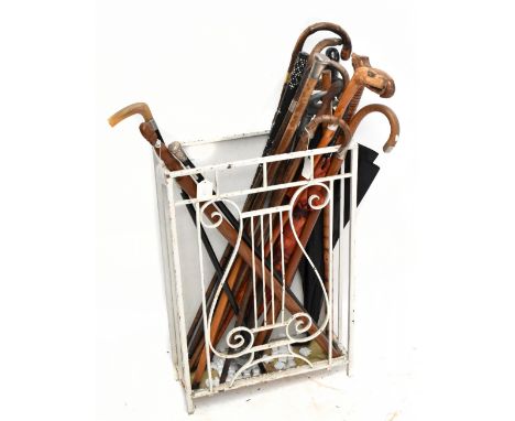 A white painted metal stick stand, with lyre shaped front, height 69cm, width 46cm, depth 16.5cm, with a selection of walking