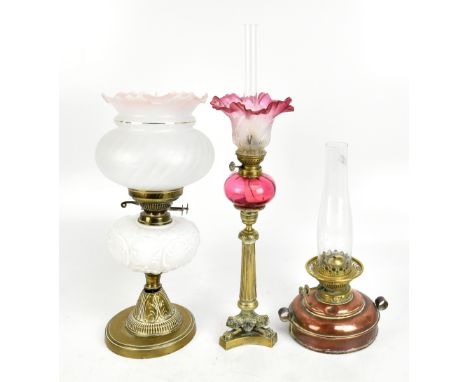 A 19th century brass oil lamp with cranberry glass reservoir raised on turned brass column supports terminating on three paw 