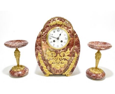 A French Art Deco rouge marble three piece clock garniture, the clock of shaped oval form with applied gilt metal floral deta