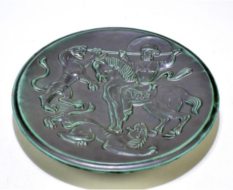 A Continental Art Pottery charger featuring a mounted warrior in combat with two lions in relief, faint monogram (possibly VE