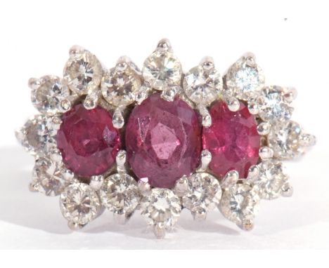 Ruby and diamond cluster ring, a design featuring three graduated oval shaped rubies, surrounded by a row of 16 small brillia