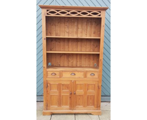 A freestanding pine display cabinet, having two adjustable open shelves, above three frieze drawers and two panelled cupboard