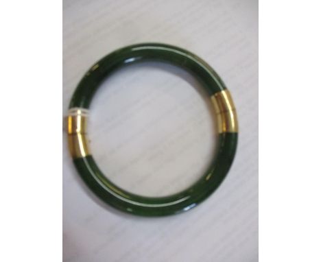 An Eastern green stone bangle, possibly Jade A/F, having a yellow metal fastening, hinge and safety, chain stamped 14k to the