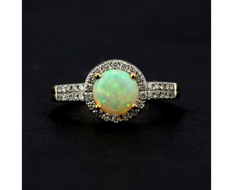 A hallmarked 18ct yellow gold ring set with a round cabochon opal surrounded by brilliant cut diamonds and diamond set should