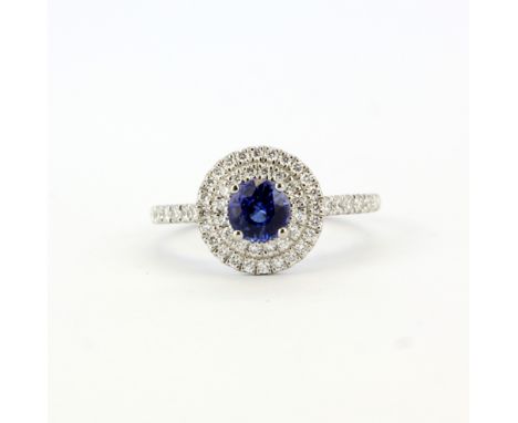 A 950 platinum ring set with a round cut sapphire, approx. 0.60ct, surrounded by diamonds and diamond set shoulders, (K.5).