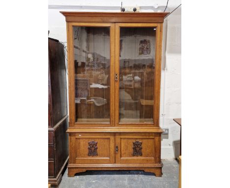 Stained oak carved bookcase, circa 1900, the double glazed doors above panelled twin cupboard doors applied with Art nouveau 