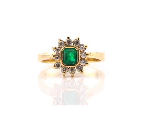 An emerald and diamond cluster ring, featuring an emerald with an intense green colour collet set in a yellow precious metal 