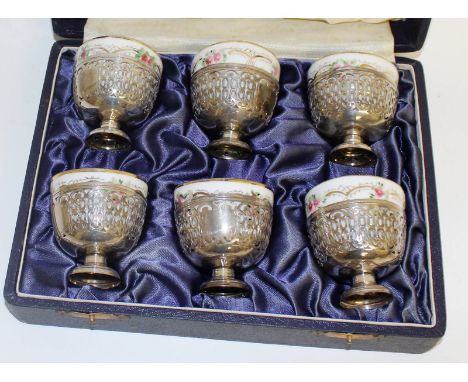 A set of six Russian porcelain vodka cups, 5.5cms diameter, in pierced silver pedestal holders, complete in a leather case.