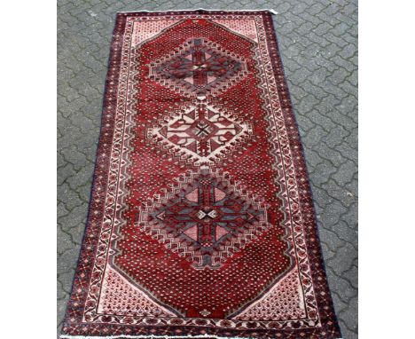 A Shiraz carpet, red ground with three large central medallions within pelmet design border. 9ft 8ins x 4ft 8ins.