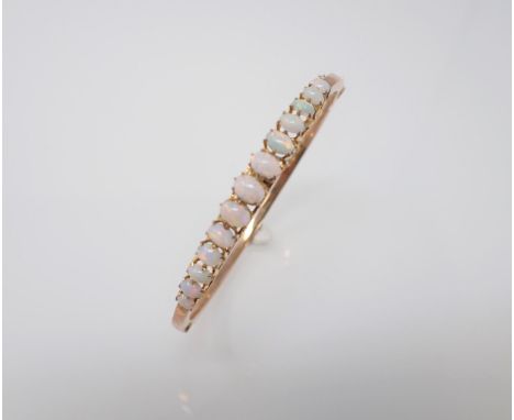 An Opal hinged Bangle the front claw-set thirteen graduated oval opal cabochons in 9ct gold, approx 6.20gms 