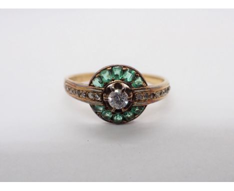A Cluster Ring claw-set white stone within step-cut emeralds and rose-cut diamonds in bands of white enamel, some losses to e