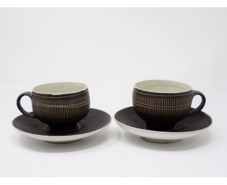 Two Lucie Rie Cups and Saucer in a brown glaze with cream trellis designs, loop handles to the bulbous bowl, on cup has damag