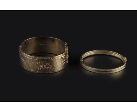 TWO HINGED BANGLES, each of oval form, the first with floral and foliate engraved decoration, 9ct gold and wax filled, the se
