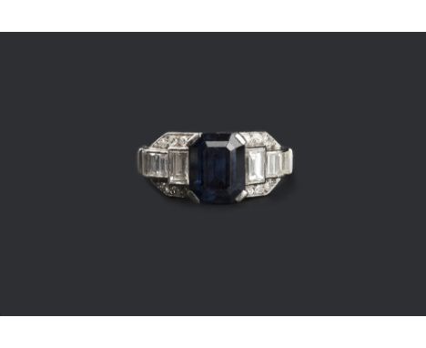 AN ART DECO STYLE SAPPHIRE AND DIAMOND DRESS RING, the rectangular step-cut sapphire with canted corners, claw set to a tiere