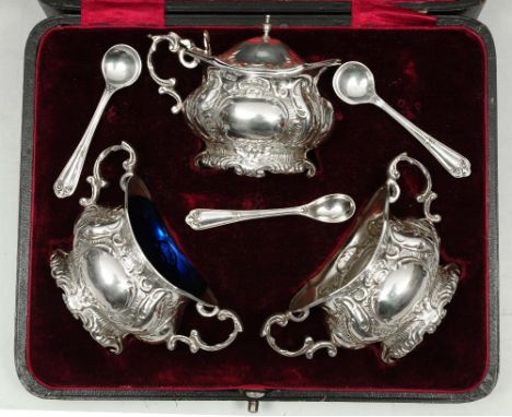 AN EDWARDIAN THREE PIECE SILVER CRUET SET, oval shaped mustard pot heavily chased with scroll and shell decoration, cast doub