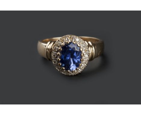 A SAPPHIRE AND DIAMOND CLUSTER RING, the oval mixed-cut sapphire claw set within a brilliant-cut diamond set border, between 