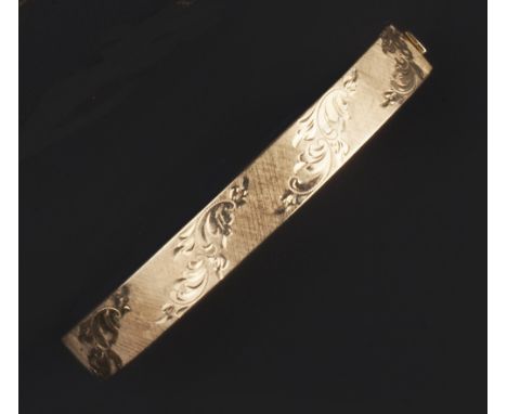 A 9CT GOLD BANGLE, of hinged oval form, decorated with foliate scrolls to a textured ground, inner diameter 6.3cm